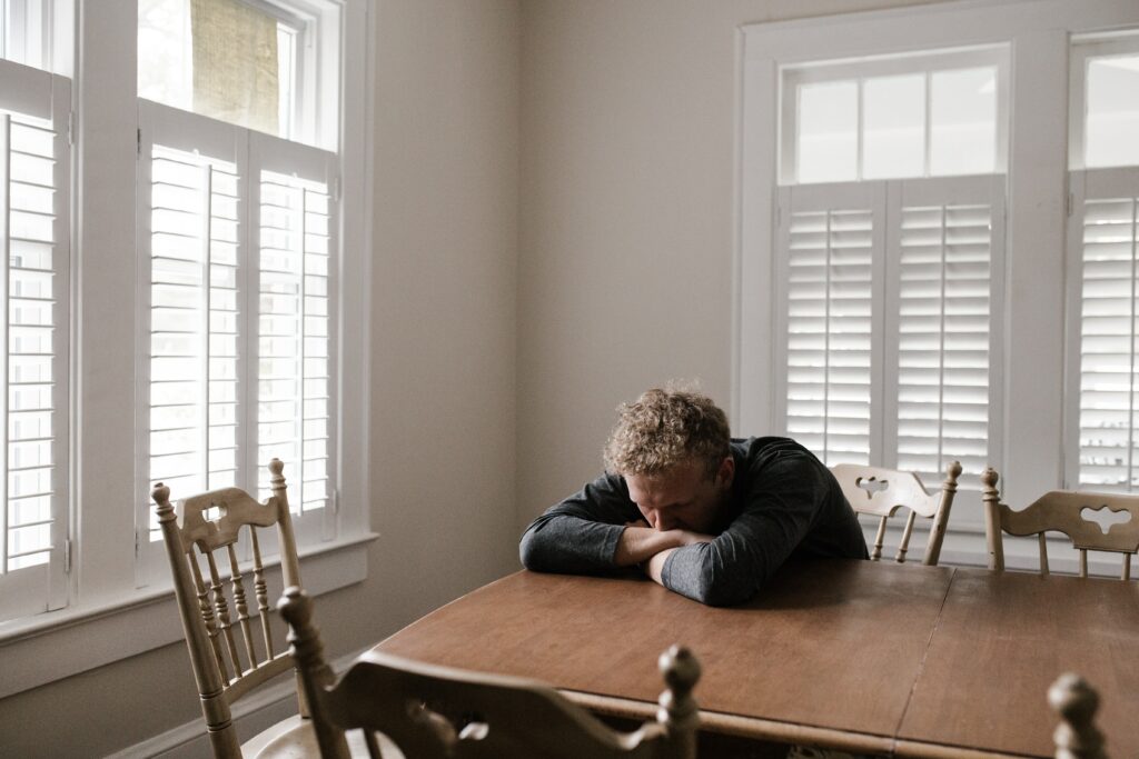 Man sitting at table with arms and head on table 