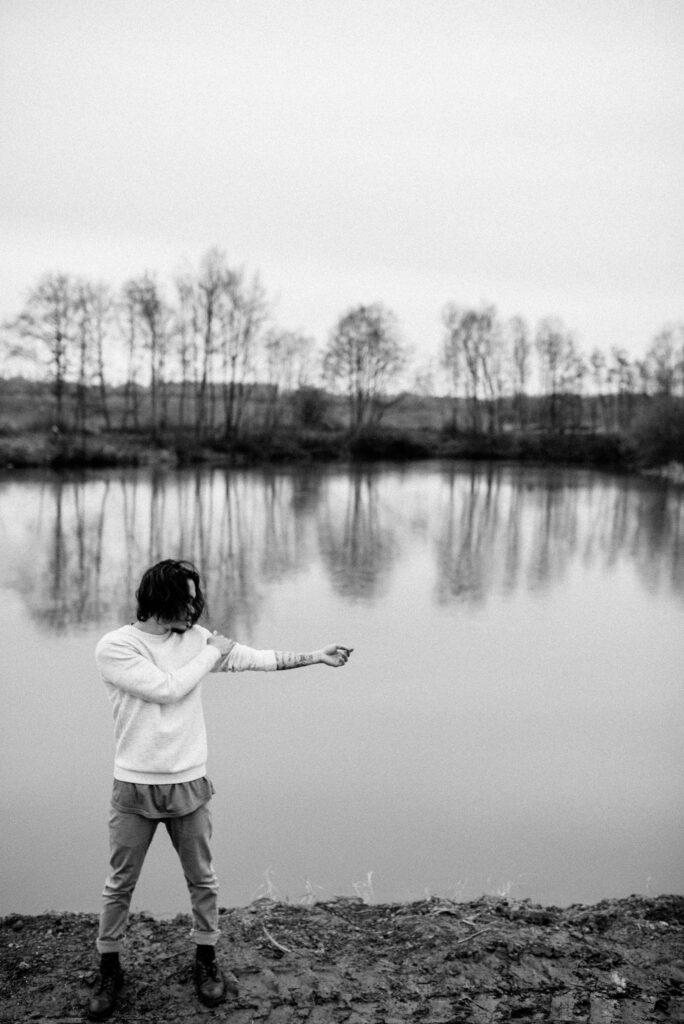 Man standing by a lake with arm stretched out