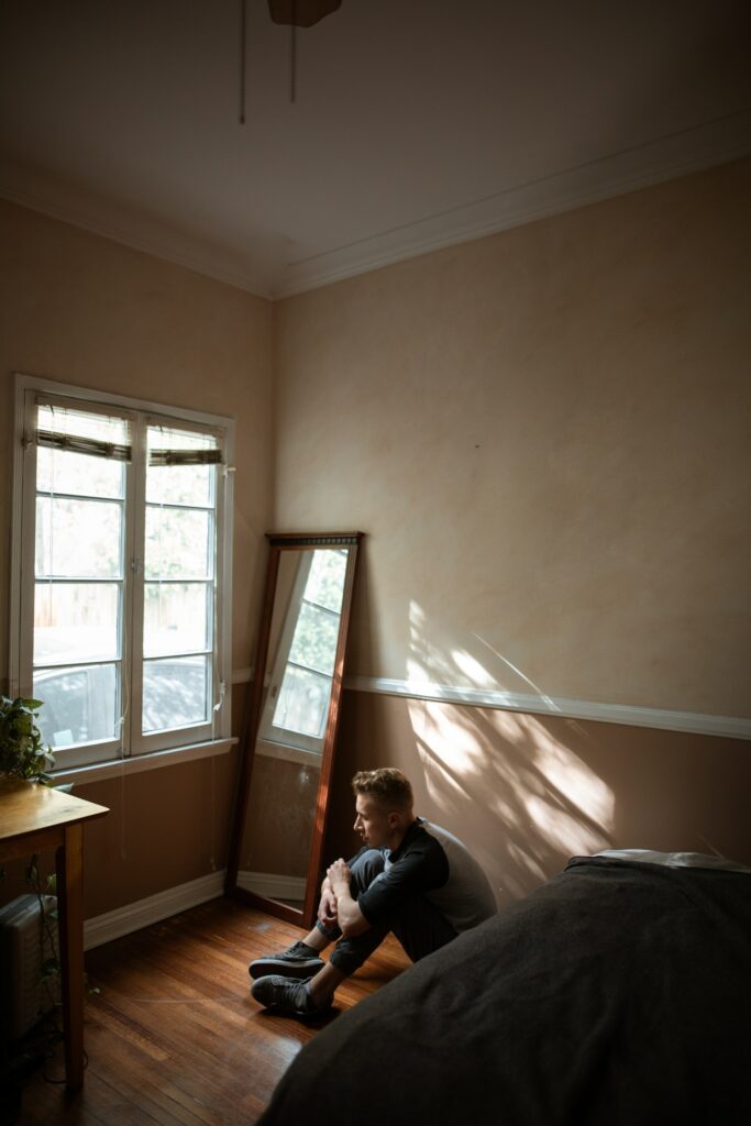 Young man sitting curled up on bedroom floor