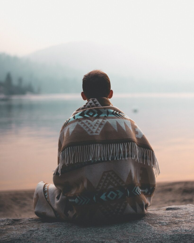 Person sitting on a log by a lake 