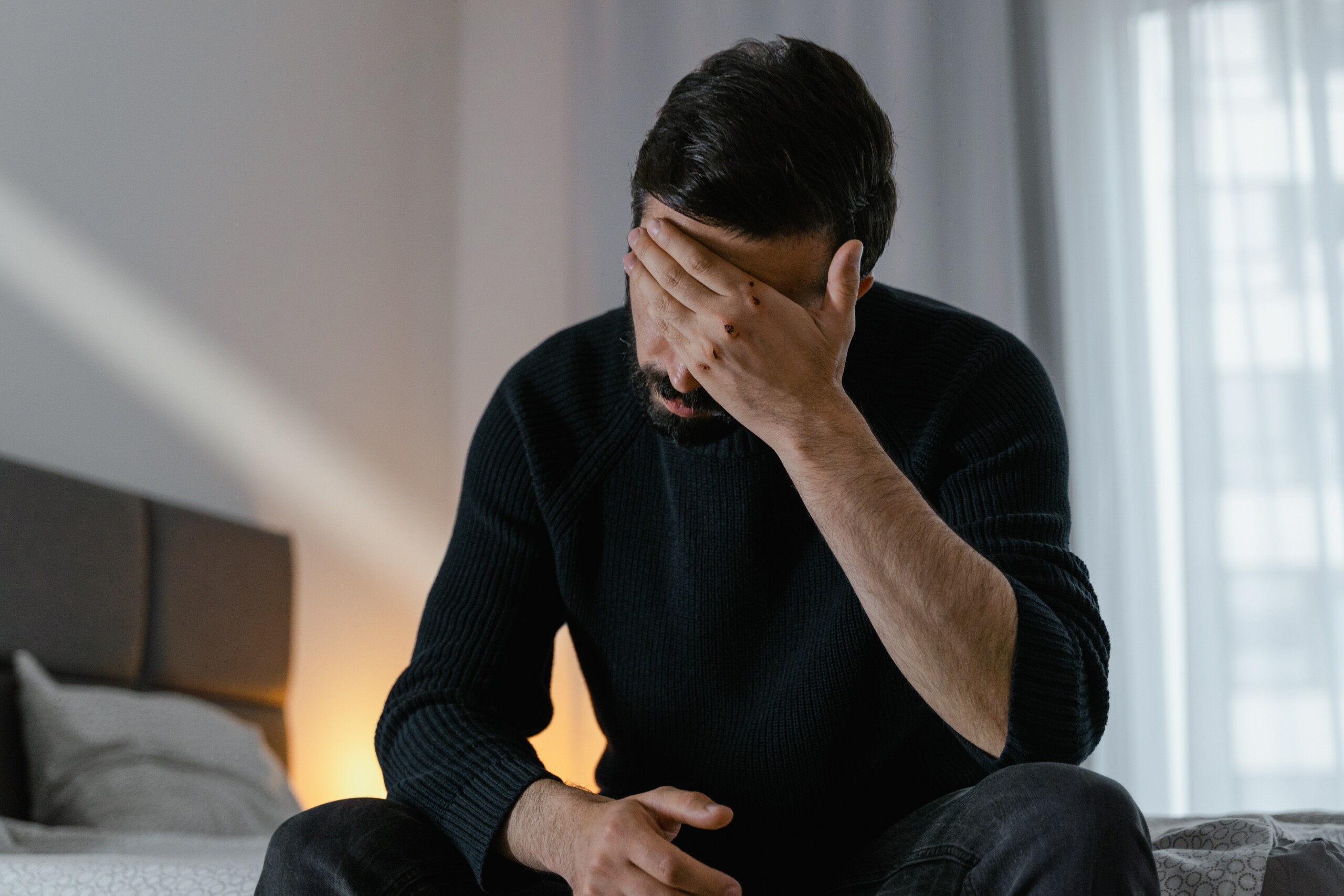 Man sitting on bedside experiencing a headache 